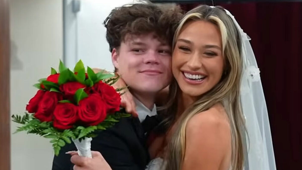 Adult star and YouTube prankster husband smiling and embracing, bride holding a bouquet of red roses on wedding day.