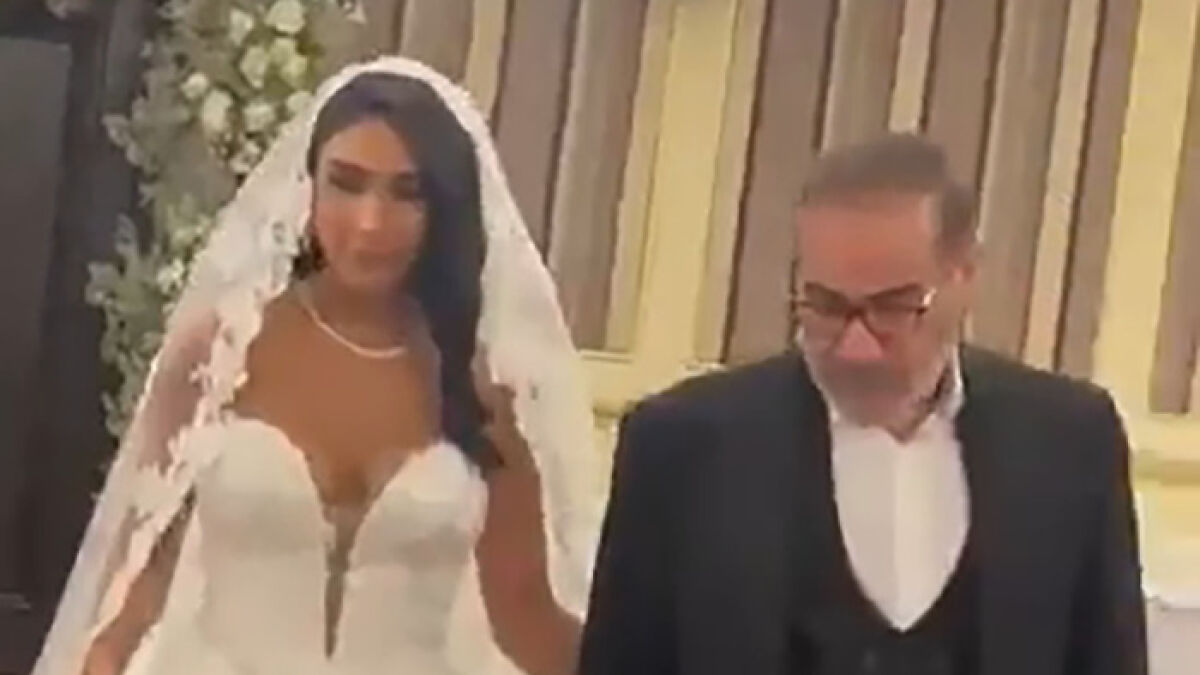 Bride in a risquu00e9 wedding dress with headscarf surveillance controversy, accompanied by an older man in formal attire.