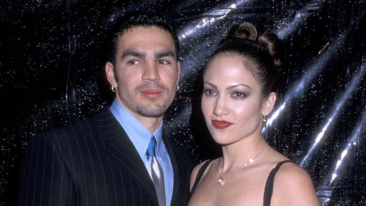 Jennifer Lopez with her ex-husband, both dressed formally, posing against a dark backdrop at an event.