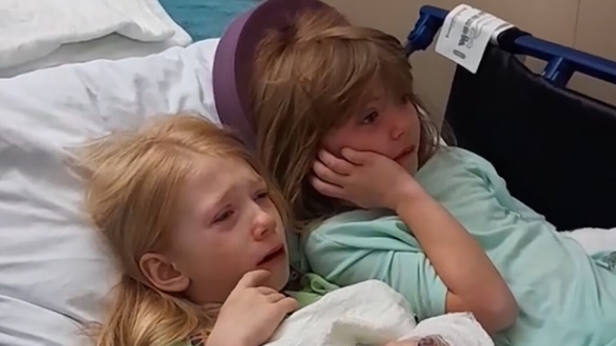 Two little sisters needing surgery lying on a hospital bed showing a heartmelting gesture by hospital staff.