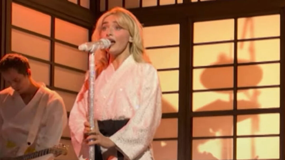 Sabrina Carpenter singing on SNL stage in a white outfit amid a set inspired by traditional Asian cultural elements.