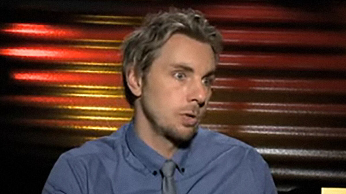Dax Shepard wearing blue shirt and gray tie, speaking during an interview about his old hitting joke about Kristen Bell.
