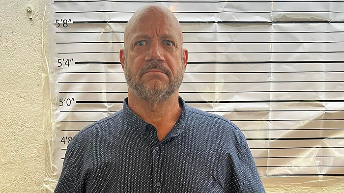 Man with beard standing in front of height chart, related to Americau2019s most notorious jewel thief and smuggling trick.