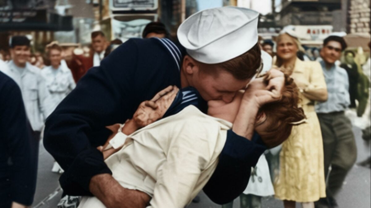 Colorization artist restores color on vintage black-and-white photograph of sailor kissing woman in crowded street.