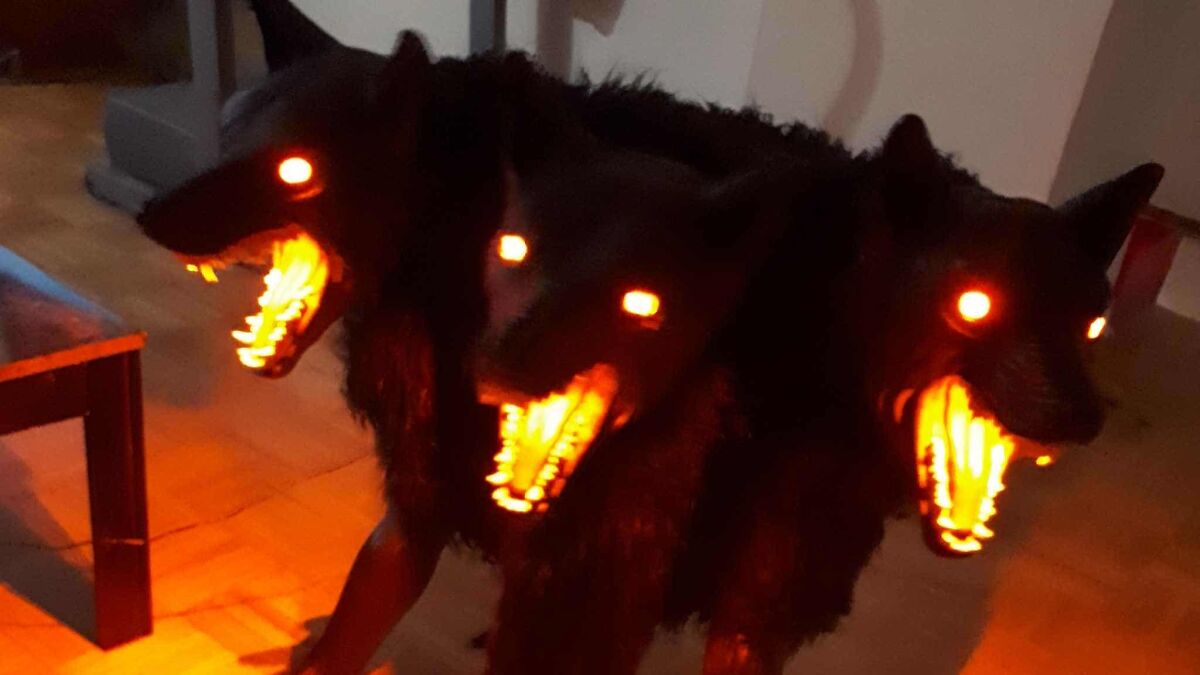 Three-headed black dog with glowing eyes and fiery mouths indoors, creating a spooky animal photo effect.