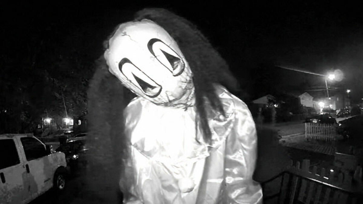 Masked figure in a disturbing doorbell prank captured on night security camera with dark neighborhood background.