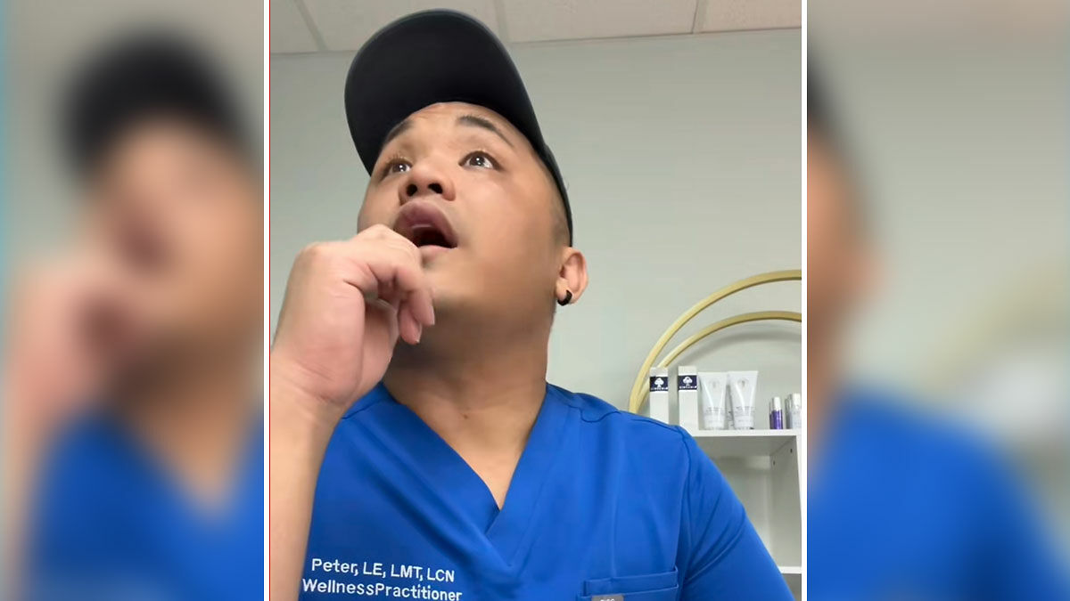 Man in blue scrubs reacting during aesthetician interaction about booking issue in a wellness clinic setting.