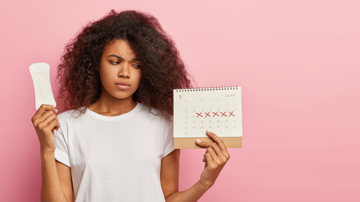 Young woman holding sanitary pad and calendar with marked dates representing period days on pink background