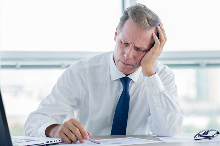 Stressed businessman in white shirt and blue tie reviewing paperwork, reflecting coworkers scammed at superior’s wife’s show. Stressed businessman in white shirt and blue tie reviewing paperwork, reflecting coworkers scammed at superior’s wife’s show.