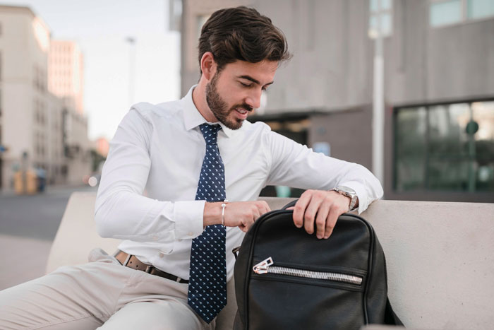 Man in white shirt and tie snooping around in a black purse outdoors, illustrating coworker snoops around in woman’s purse scenario. Man in white shirt and tie snooping around in a black purse outdoors, illustrating coworker snoops around in woman’s purse scenario.