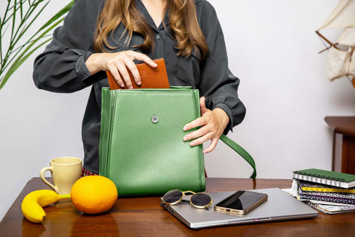 Woman opening green purse on desk with fruit, sunglasses, and laptop illustrating coworker snooping around incident. Woman opening green purse on desk with fruit, sunglasses, and laptop illustrating coworker snooping around incident.