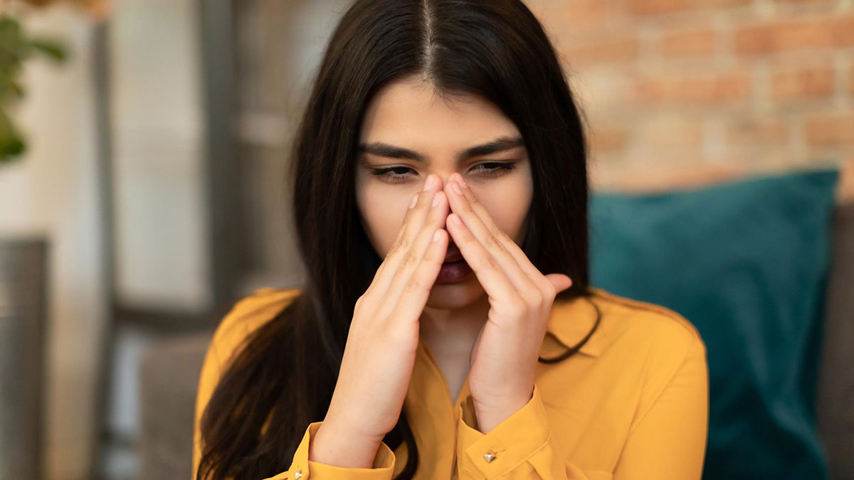 Woman covering nose with her hands indoors, reacting to coworker sensitive smells and avoiding washing hands.