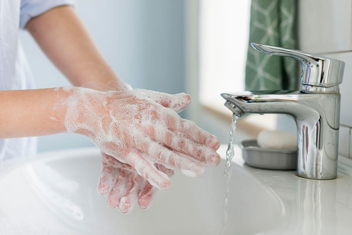Person washing hands with soap under running water, addressing coworker sensitive smells and hand hygiene concerns.