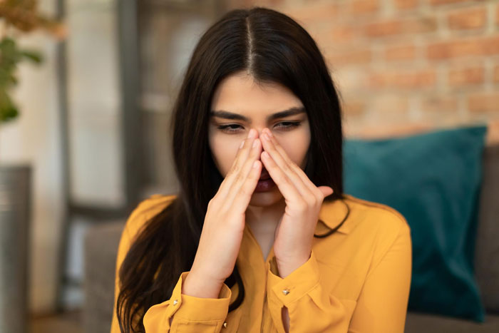 Young woman in a yellow shirt covering her nose, reacting to coworker sensitive smells in an indoor office setting