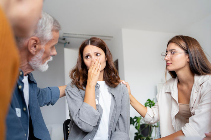 A woman covers her nose reacting to coworker sensitive smells while colleagues offer comfort in an office setting.