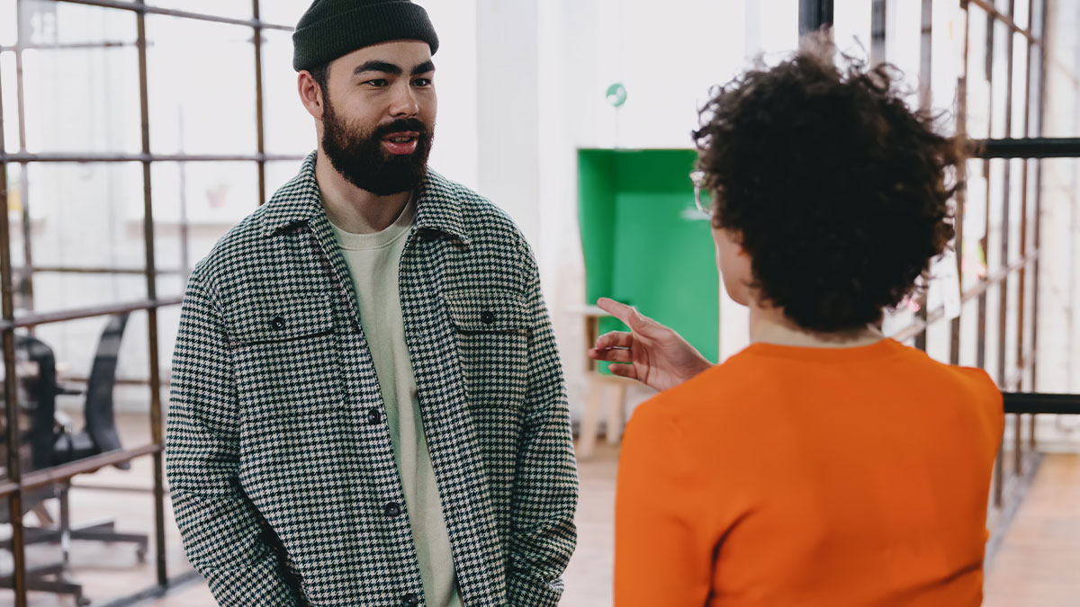 Man and woman talking in office, coworker asking why she wears makeup every day, sparking online debate.