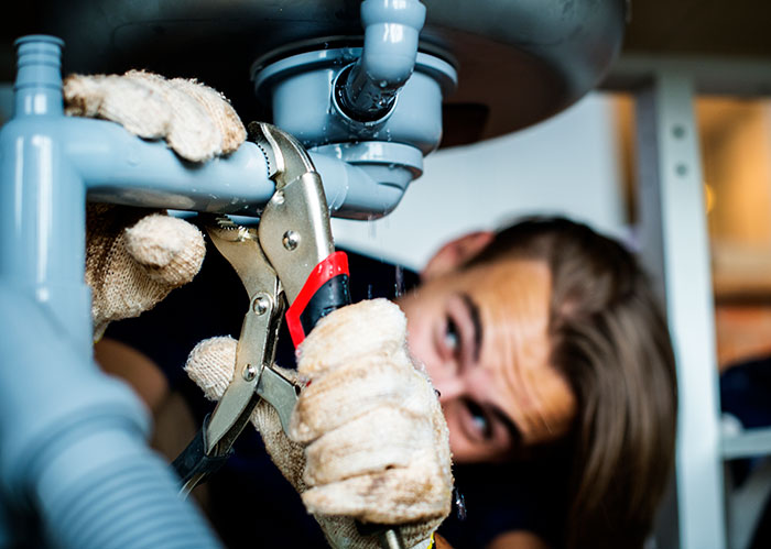 Plumber wearing gloves fixing pipes under a sink, illustrating a work nepotism scenario in a professional setting.