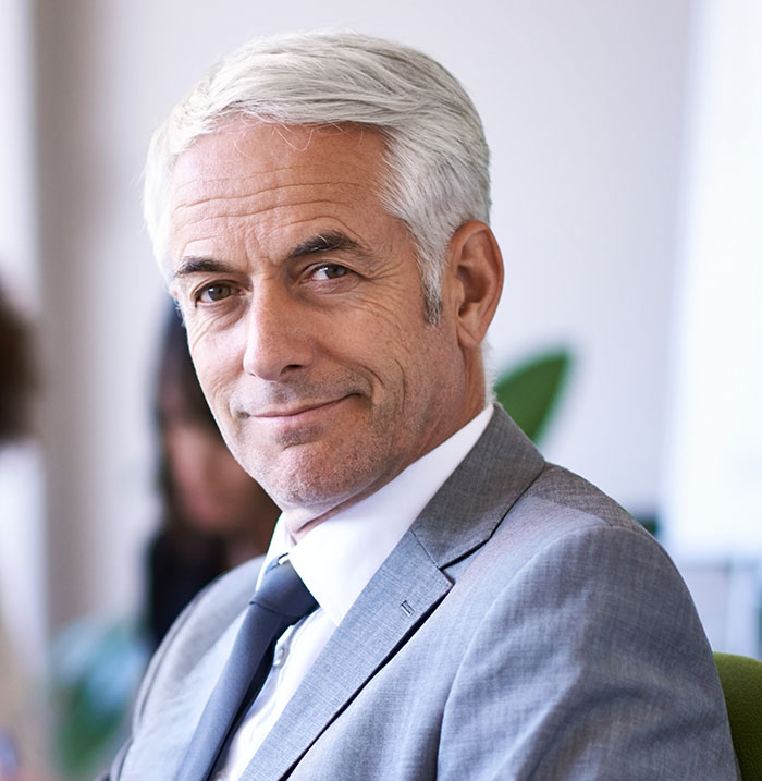 Confident businessman in a gray suit smiling in an office setting, illustrating work nepotism in professional environments.