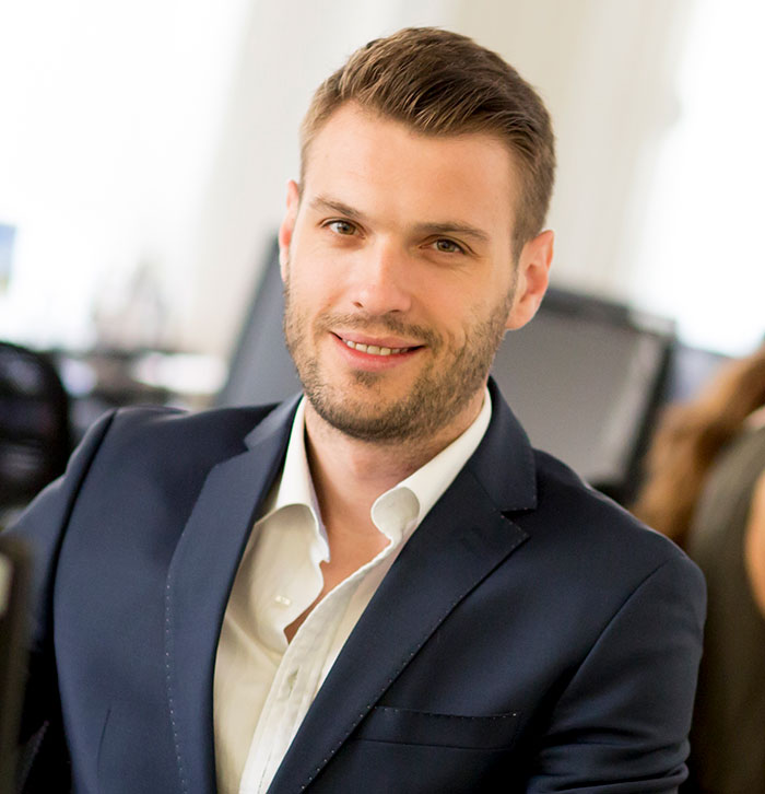 Young professional man in a suit smiling confidently, representing cases of work nepotism in a modern office setting.