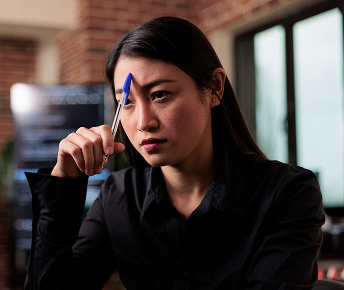 Young woman in a black shirt holding a pen to her forehead, reflecting on workplace nepotism cases she has witnessed.