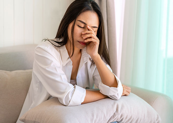 Young woman looking stressed and frustrated while sitting on a couch, reflecting on work nepotism experiences