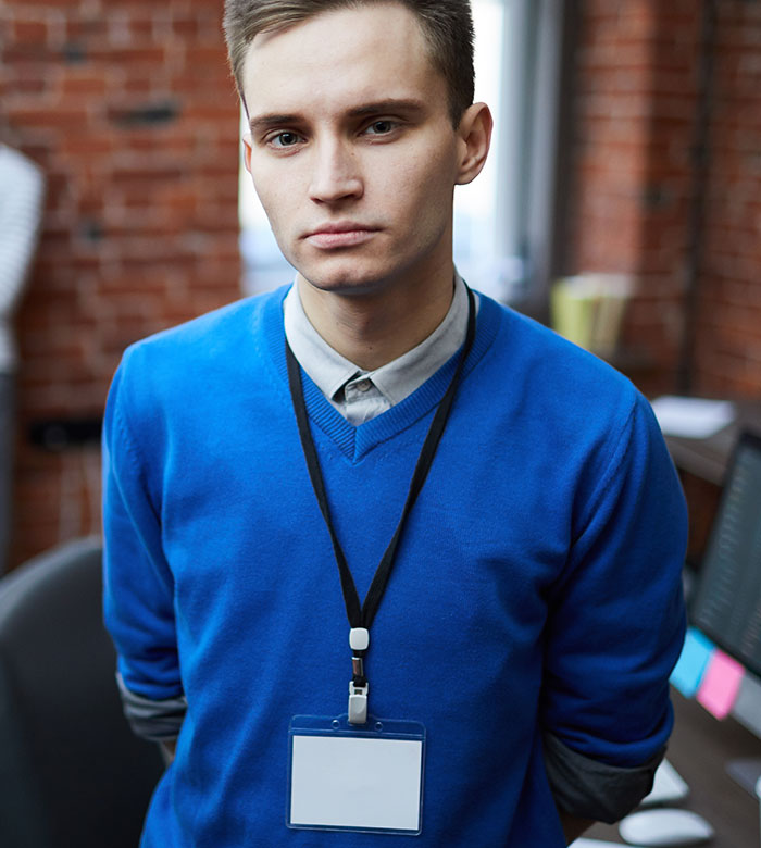 Young man wearing blue sweater and blank ID badge in office representing work nepotism cases witnessed by employees.