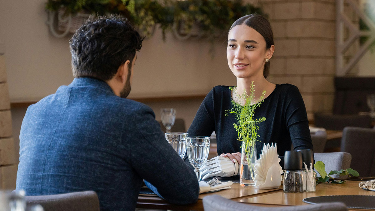 Woman with a robotic hand talking to a man at a restaurant, depicting creepy things women said or did to men.