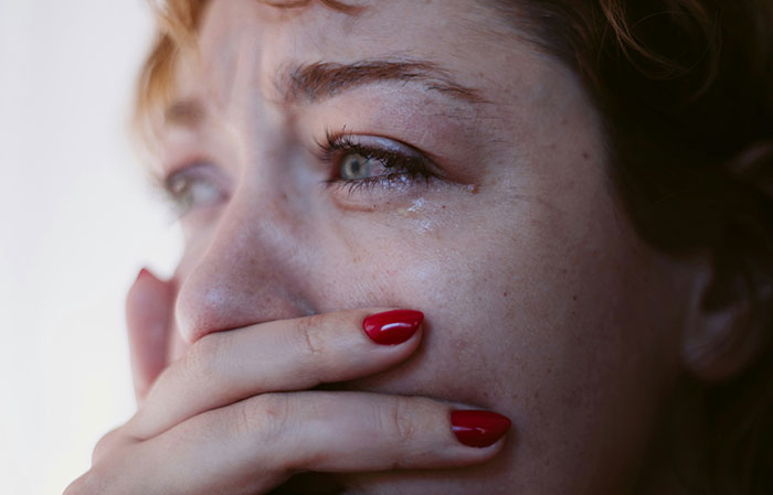 Close-up of a woman with red nail polish covering her mouth, showing fear from creepy found footage and videos.