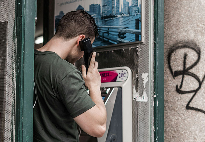 Man in a dark shirt using a public phone booth, evoking creepy found footage and chilling video themes.