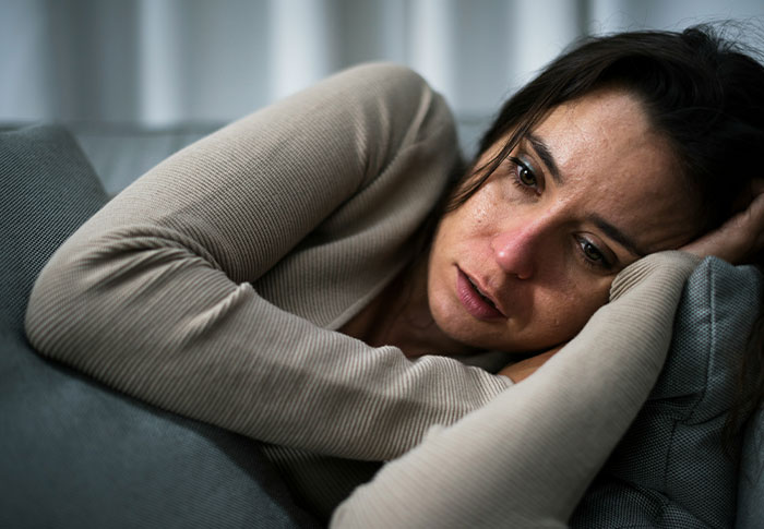 Woman lying on couch looking distressed and anxious, evoking feelings linked to creepy found footage and videos.