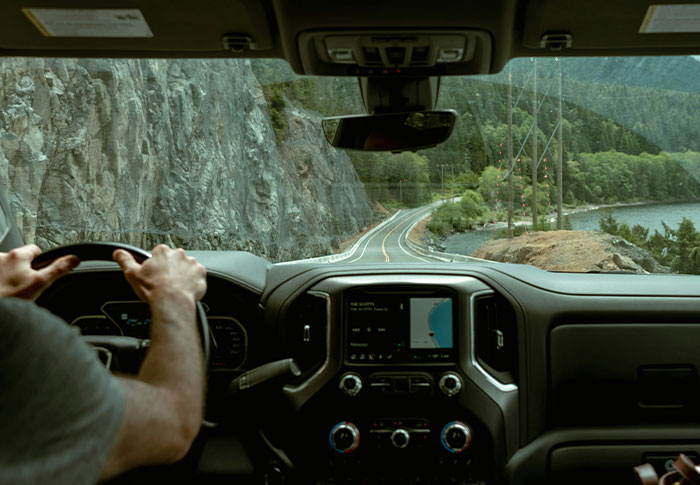 View from inside a vehicle driving along a winding road by a rocky cliff and forest, eerie found footage vibe