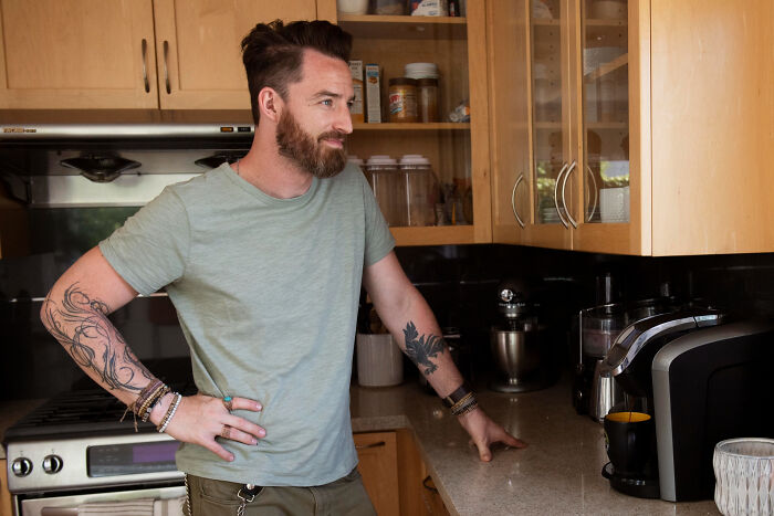Man with tattoos standing in kitchen looking to the side, illustrating creepy thing home stories atmosphere.