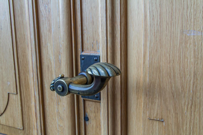 Antique brass door handle on a wooden door, evoking a creepy thing vibe in home stories setting.