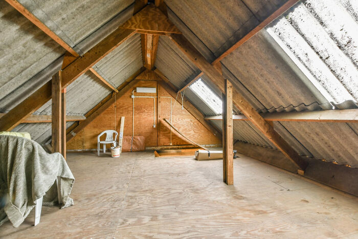 Empty attic space with exposed wooden beams, plastic chair, and scattered items hinting at creepy thing home stories.