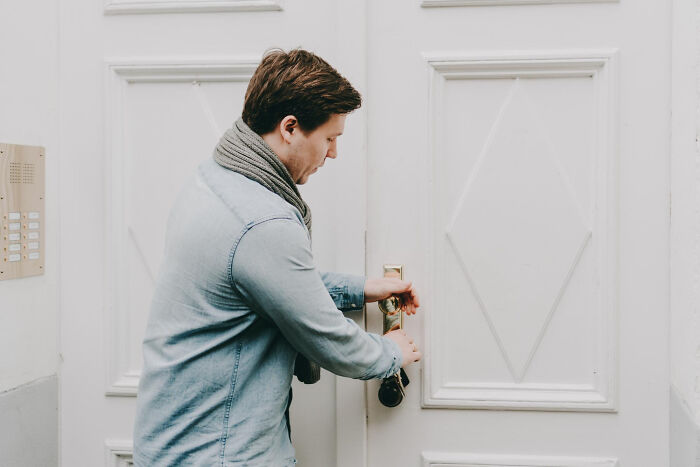 Man in a denim shirt unlocking white door, creating a suspenseful moment in creepy thing home stories.