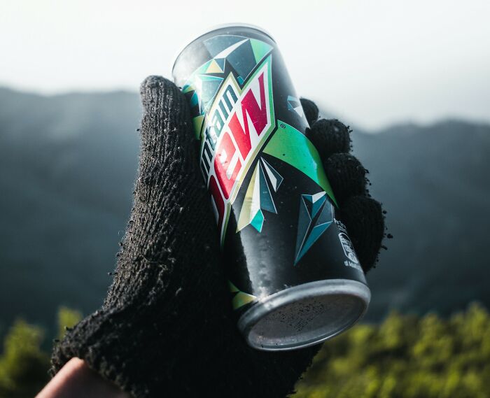 Hand wearing black glove holding a Mountain Dew can outdoors with a blurred mountainous background, creepy thing home stories.