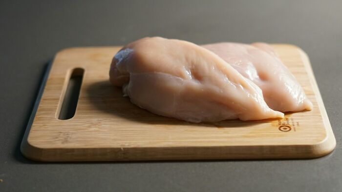 Raw chicken breasts on a wooden cutting board, an ingredient that could be used in shrimp jello recipes or unusual dishes.