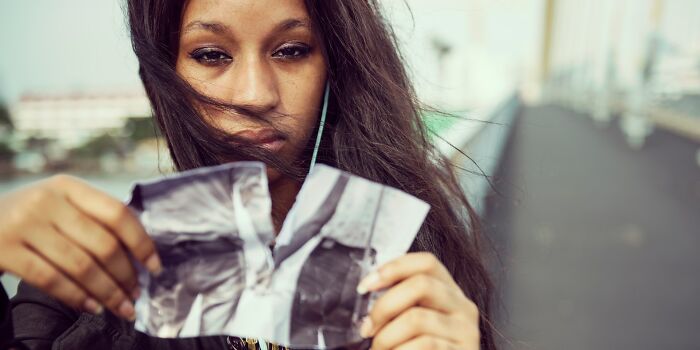 Young woman outdoors holding a torn photo, expressing emotion related to relationship advice and couple challenges.