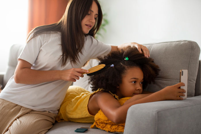 Mom brushing out biracial daughter's curls on a couch, highlighting biracial hair care and whitewashing controversy. Mom brushing out biracial daughter's curls on a couch, highlighting biracial hair care and whitewashing controversy.
