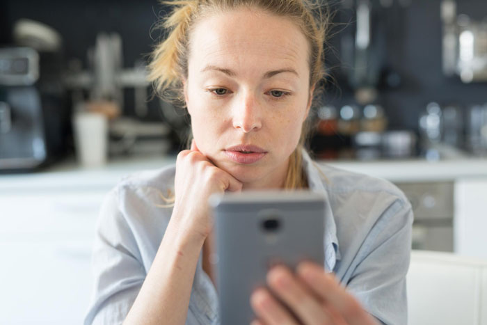 Woman with concerned expression looking at smartphone focusing on mom whitewashing biracial daughter's curls debate online. Woman with concerned expression looking at smartphone focusing on mom whitewashing biracial daughter's curls debate online.