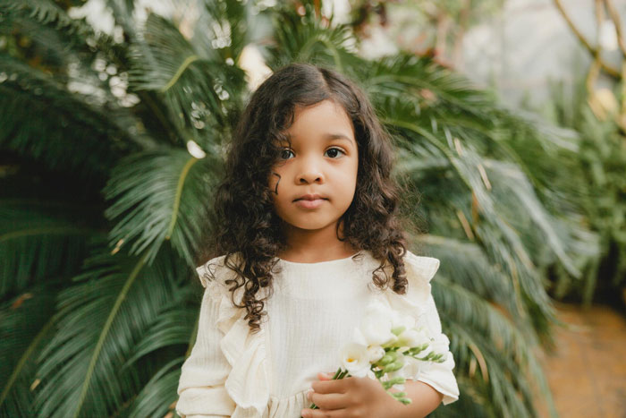 Biracial daughter with curly hair holding white flowers outdoors surrounded by green foliage. Biracial daughter with curly hair holding white flowers outdoors surrounded by green foliage.