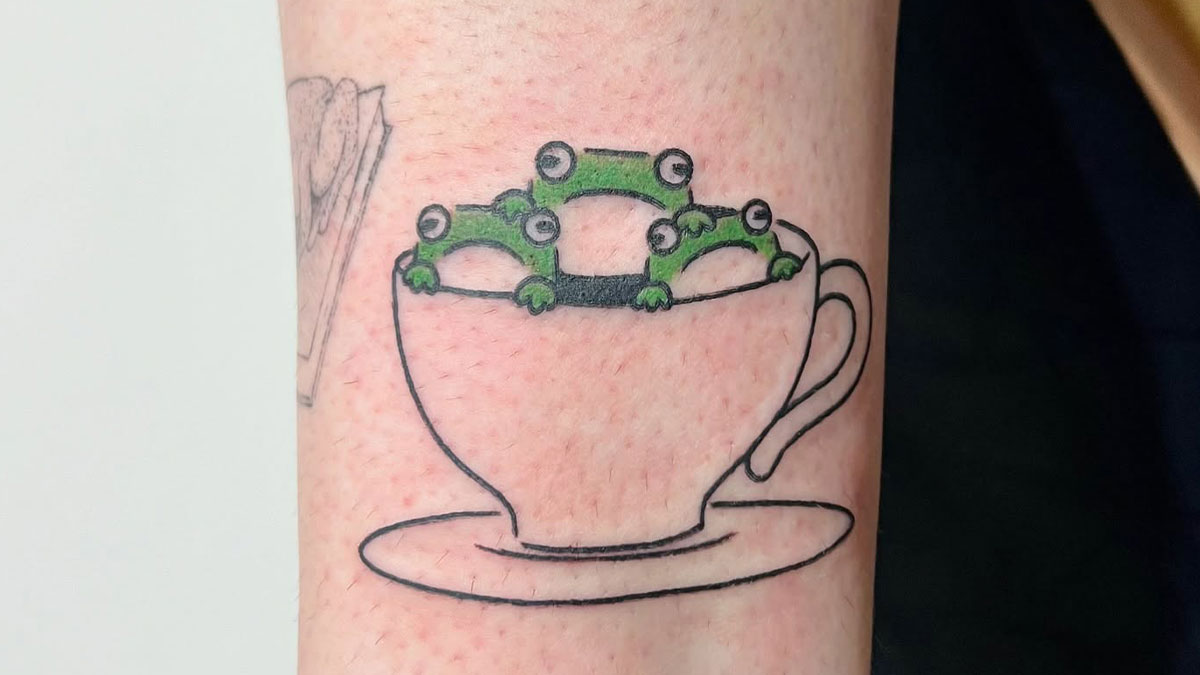 Tattoo of adorable frogs peeking out of a teacup, showcasing cute animal ink art by a Korean tattoo artist.