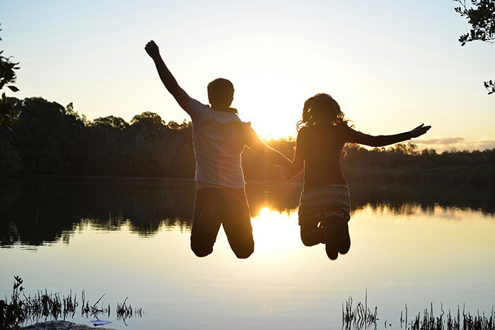 Silhouetted couple holding hands and jumping by a lakeside at sunset, symbolizing rejection and new dating after bestie drama. Silhouetted couple holding hands and jumping by a lakeside at sunset, symbolizing rejection and new dating after bestie drama.