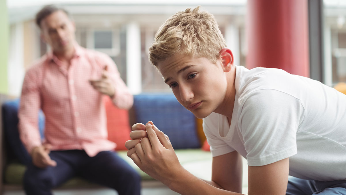 Teen looking upset and frustrated while dad talks in the background after a cake fail moment between them