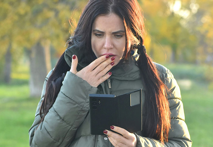 Woman in a green jacket looking shocked at her phone, capturing emotions related to rejection and dating after heartbreak. Woman in a green jacket looking shocked at her phone, capturing emotions related to rejection and dating after heartbreak.