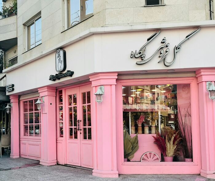 Pink flower shop exterior with large windows displaying floral arrangements and decorative plants inside.