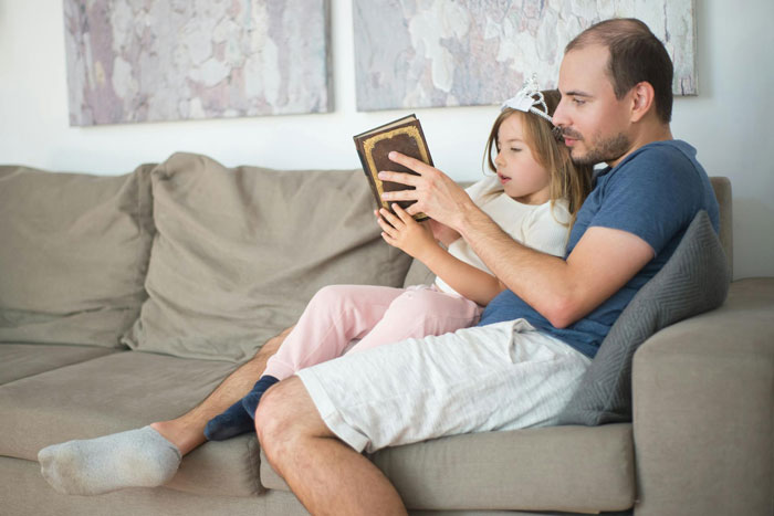 Man reading a book with his young daughter on the couch, highlighting challenges dating men with kids again. Man reading a book with his young daughter on the couch, highlighting challenges dating men with kids again.