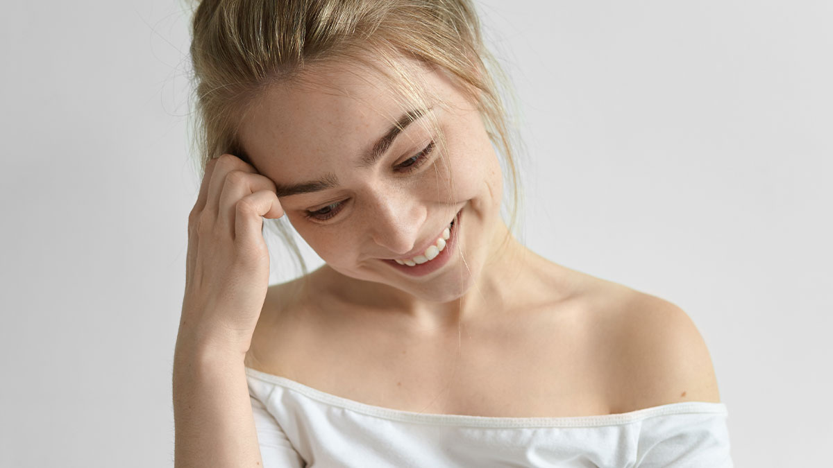 A smiling daycare worker in a white off-shoulder shirt, reflecting on unexpected family secrets she's heard.