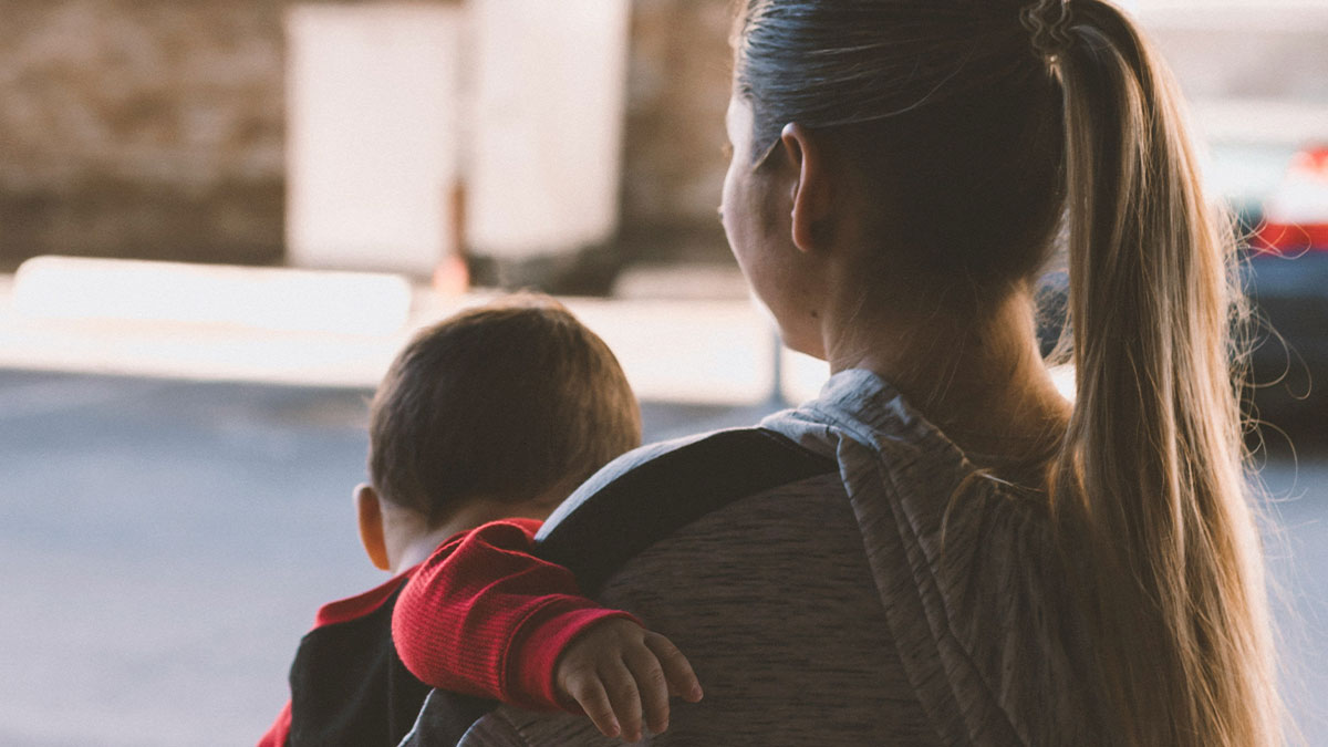 Woman carrying child on her back outdoors, representing the villain in someone elseu2019s story theme.