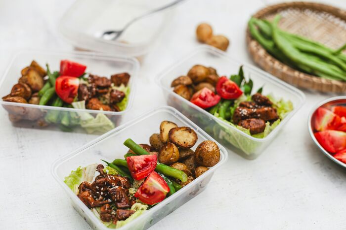 Meal prep containers with cooked potatoes, green beans, tomatoes, and seasoned meat showcasing simple life hacks for easy cooking.
